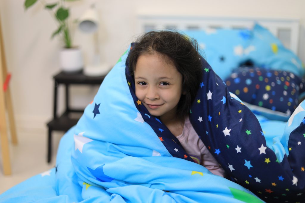 Young girl hiding under space themed weighted blanket